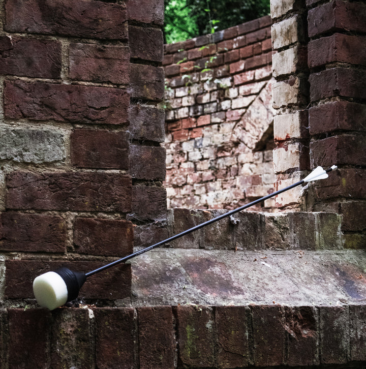 Black foam headed arrow for larp leaning against a brick wall.
