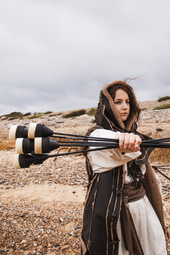 Person in historical attire holding multiple arrows on a rocky landscape