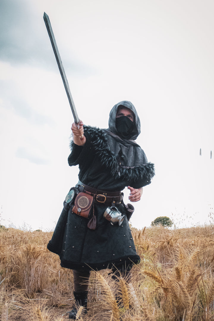Person in dark medieval attire holding a spear in a field