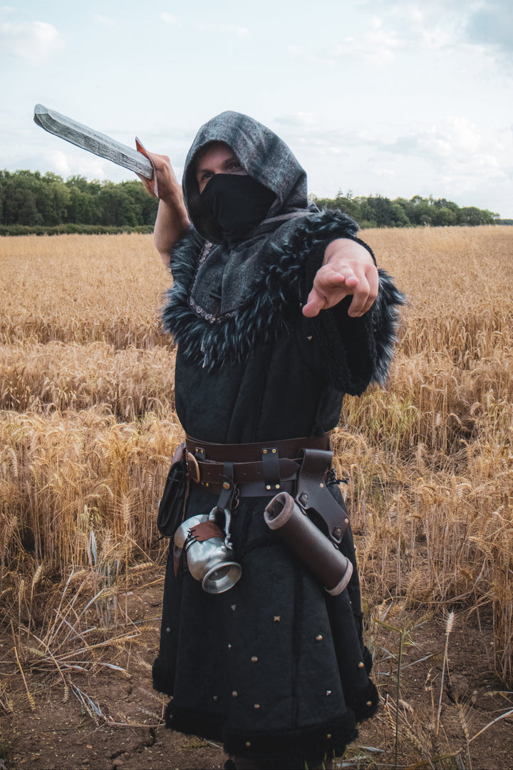 Person in a hooded cloak holding a weapon in a field