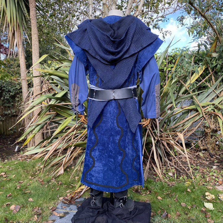 Medieval LARP costume back view, featuring a blue suede-effect panel waistcoat, wool hood, two-tone cotton tunic and wool sash. For Renaissance Faire and historical roleplay events.