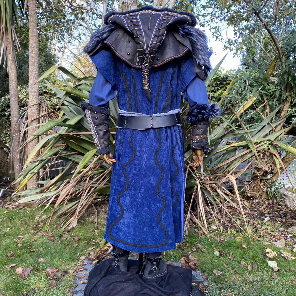 Medieval LARP costume back view, featuring a blue suede-effect panel waistcoat, black faux-leather hood and vambraces, tunic, leather belt and sash. For Renaissance Faire and historical roleplay events.