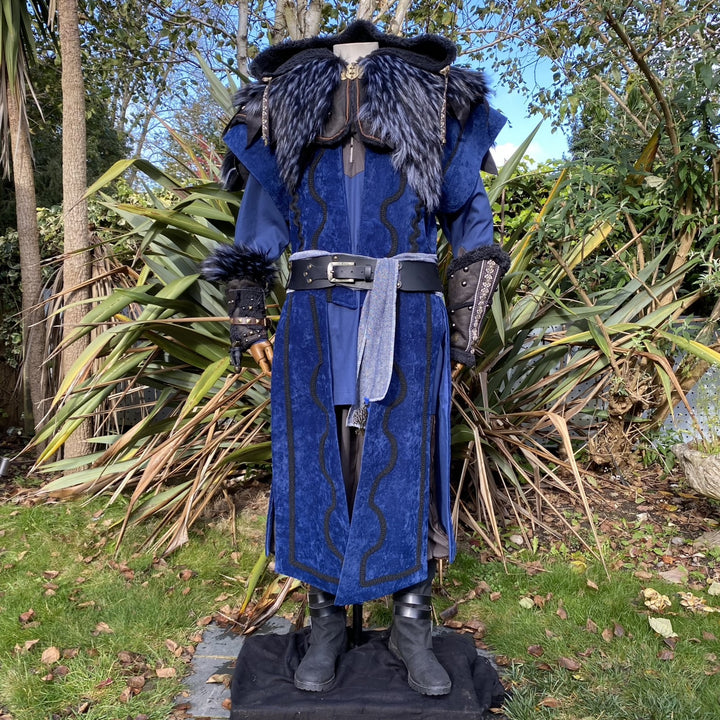 Medieval LARP costume front view, featuring a blue suede-effect panel waistcoat, black faux-leather hood and vambraces, tunic, leather belt and sash. For Renaissance Faire and historical roleplay events.