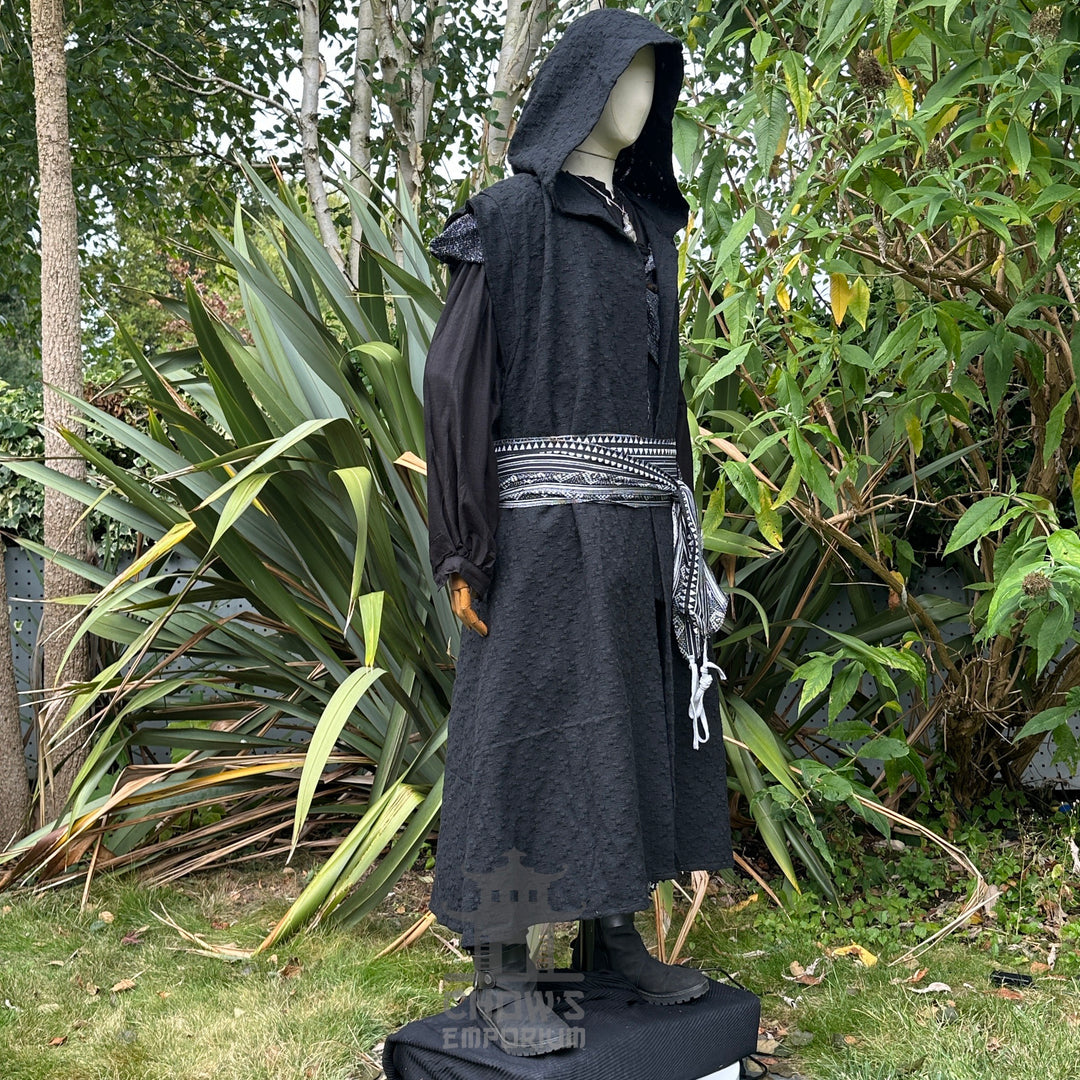 Medieval LARP costume side view featuring black sleeveless robe, hood, shirt, trousers, and sash. For Renaissance Faire and historical roleplay events.
