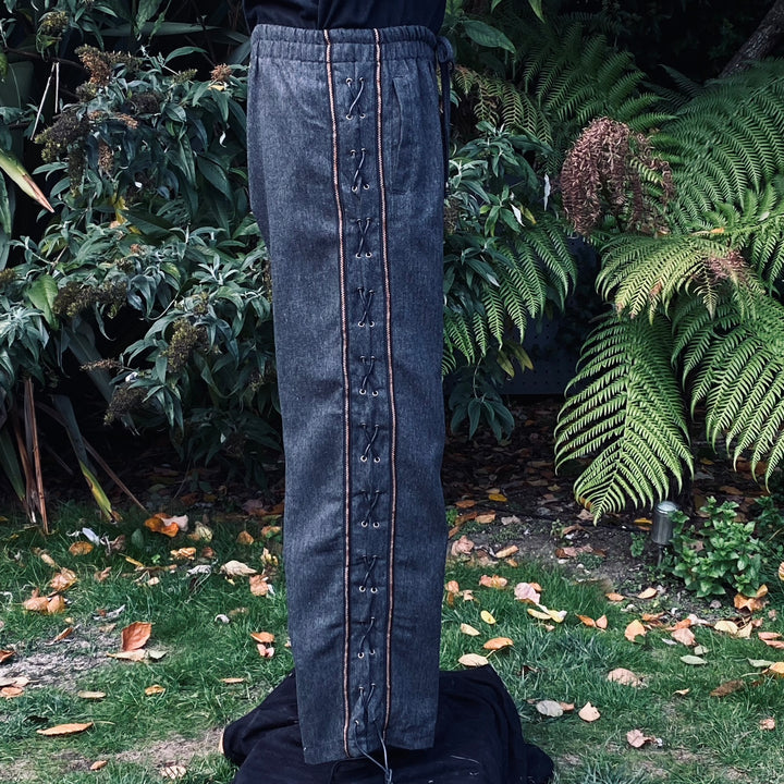 Side view of grey wool pants with wide decorative trim and cross-lace detailing no boots
