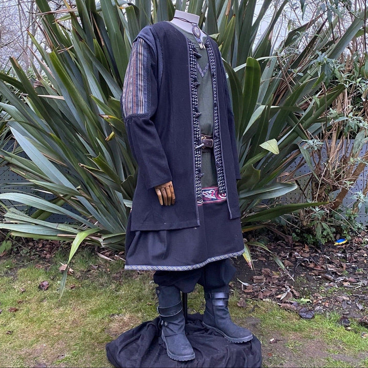 Medieval LARP costume back view, featuring a black and grey wool jacket with ornate panels, a two-tone linen tunic, and a sash. For Renaissance Faire and historical roleplay events.