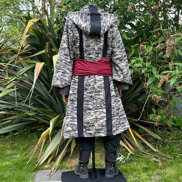 Medieval LARP costume back view, featuring brown and black hooded robe, two-tone shirt, trousers and sash. For Renaissance Faire and historical roleplay events.