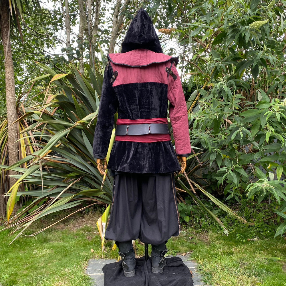 Back view of a medieval LARP costume, featuring a black and red gambeson jacket with removable sleeves, matching hood, shirt, pants, leather belt, and woolen sash. For Renaissance Faire and roleplay events.