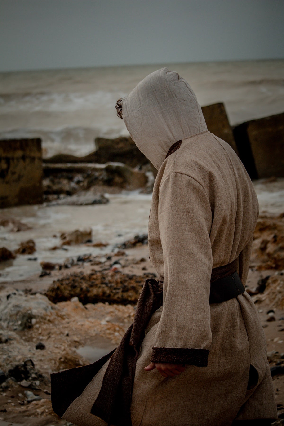 Hooded medieval shirt in natural cotton and linen, side view on beach.