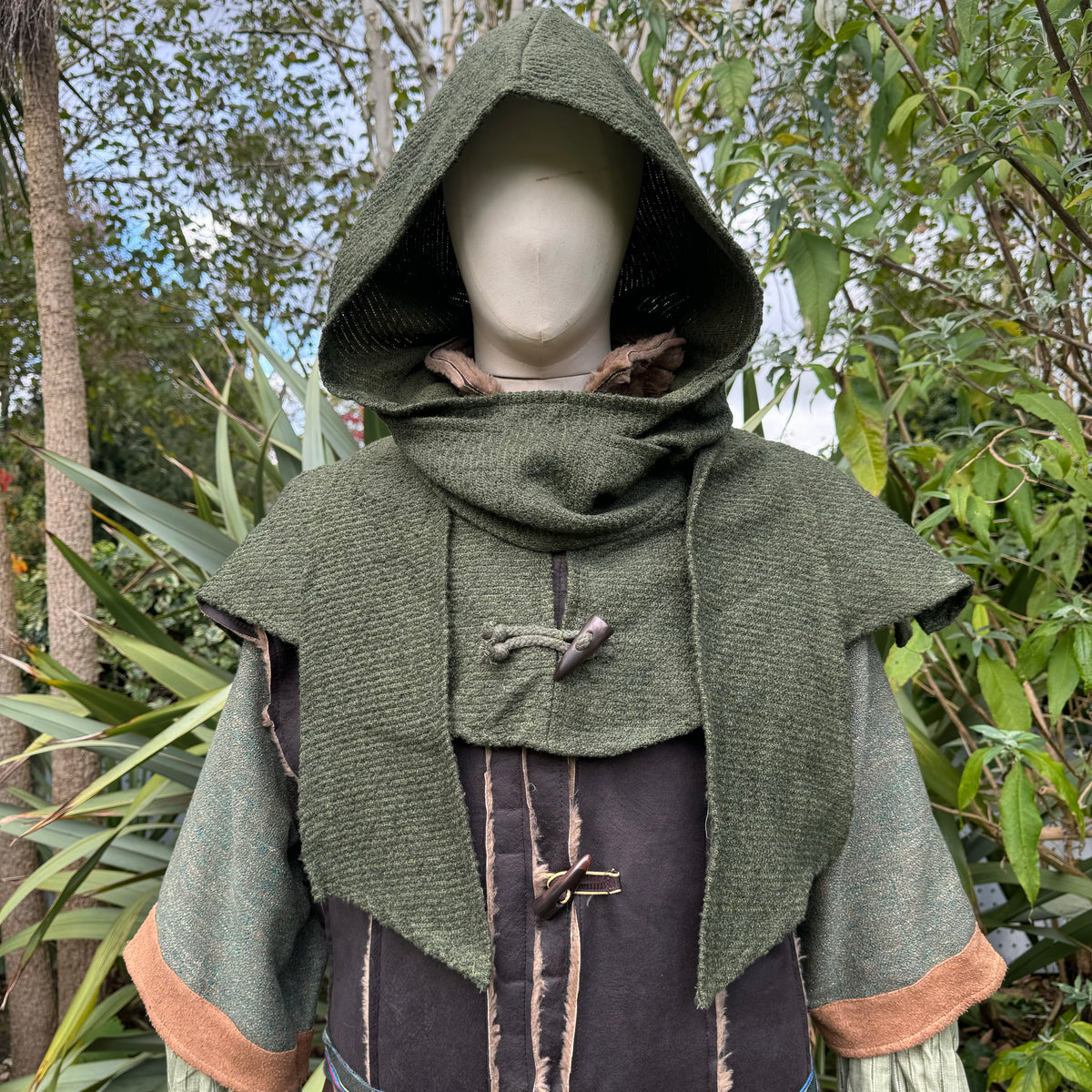 Green wool scarf hood for medieval LARP costume, front view with greenery.