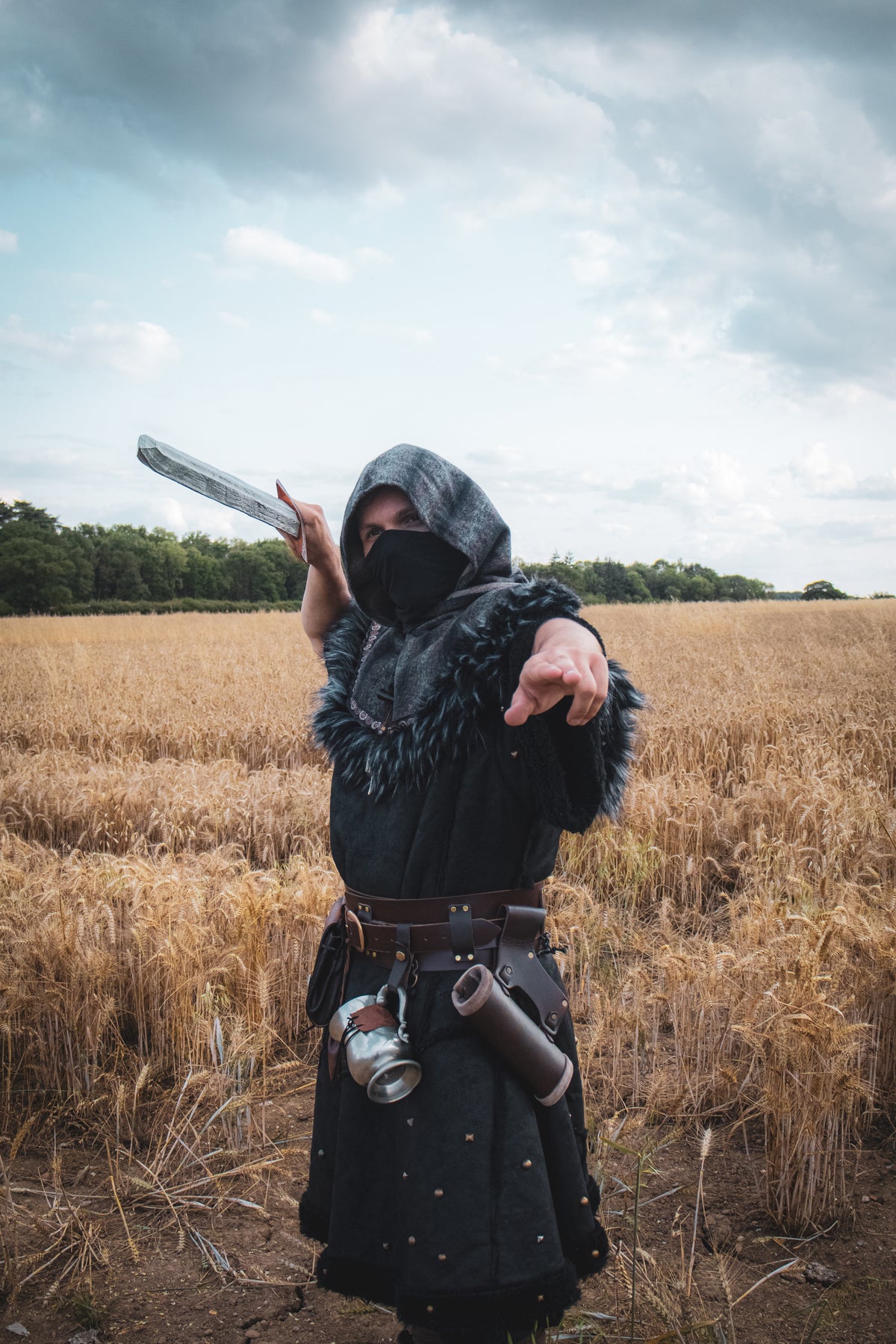 Fighter in barbarian LARP armor, black faux leather tunic and mohair hood in field.