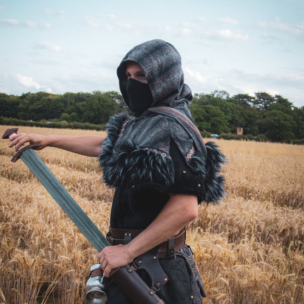 Person in medieval or fantasy costume holding a sword in a field