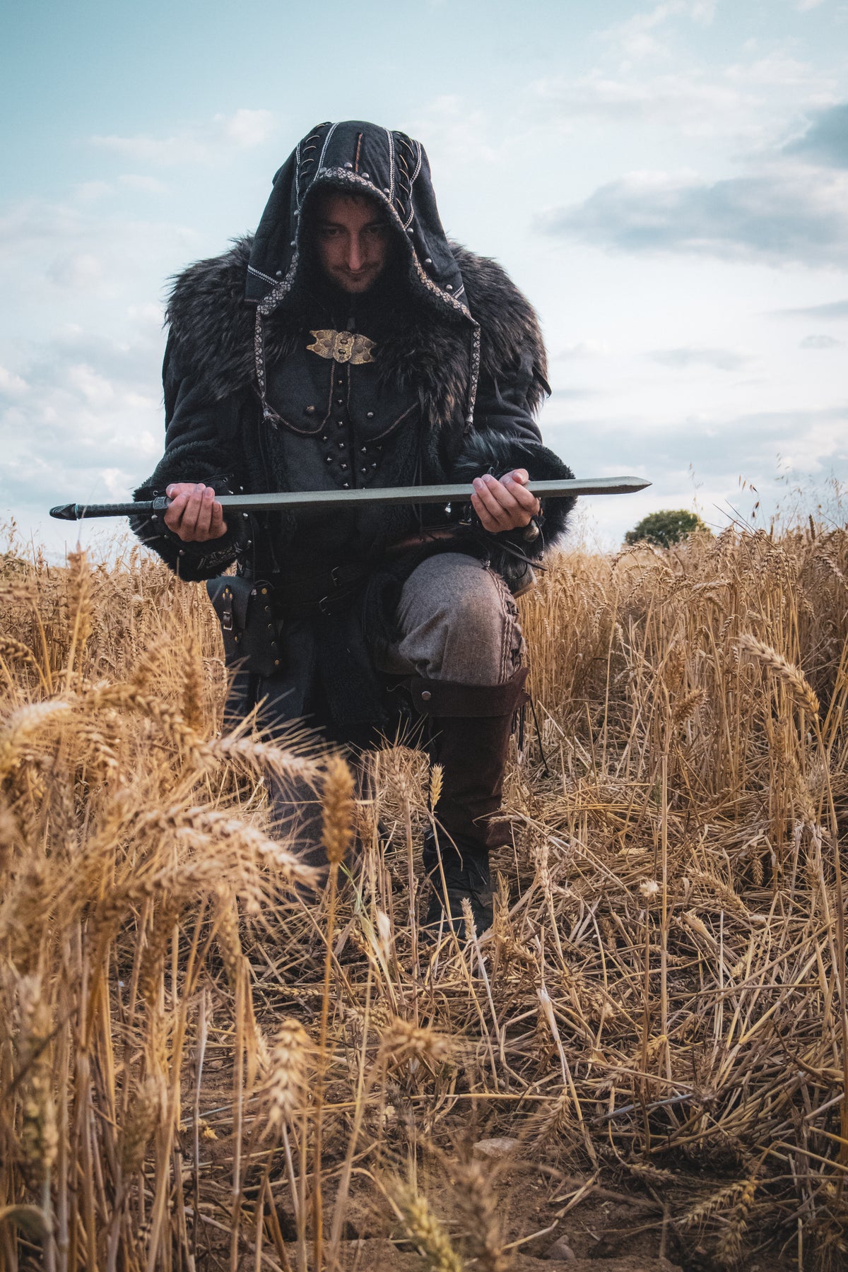 Dark warrior LARP costume with black hood, jacket, and vambraces in field.