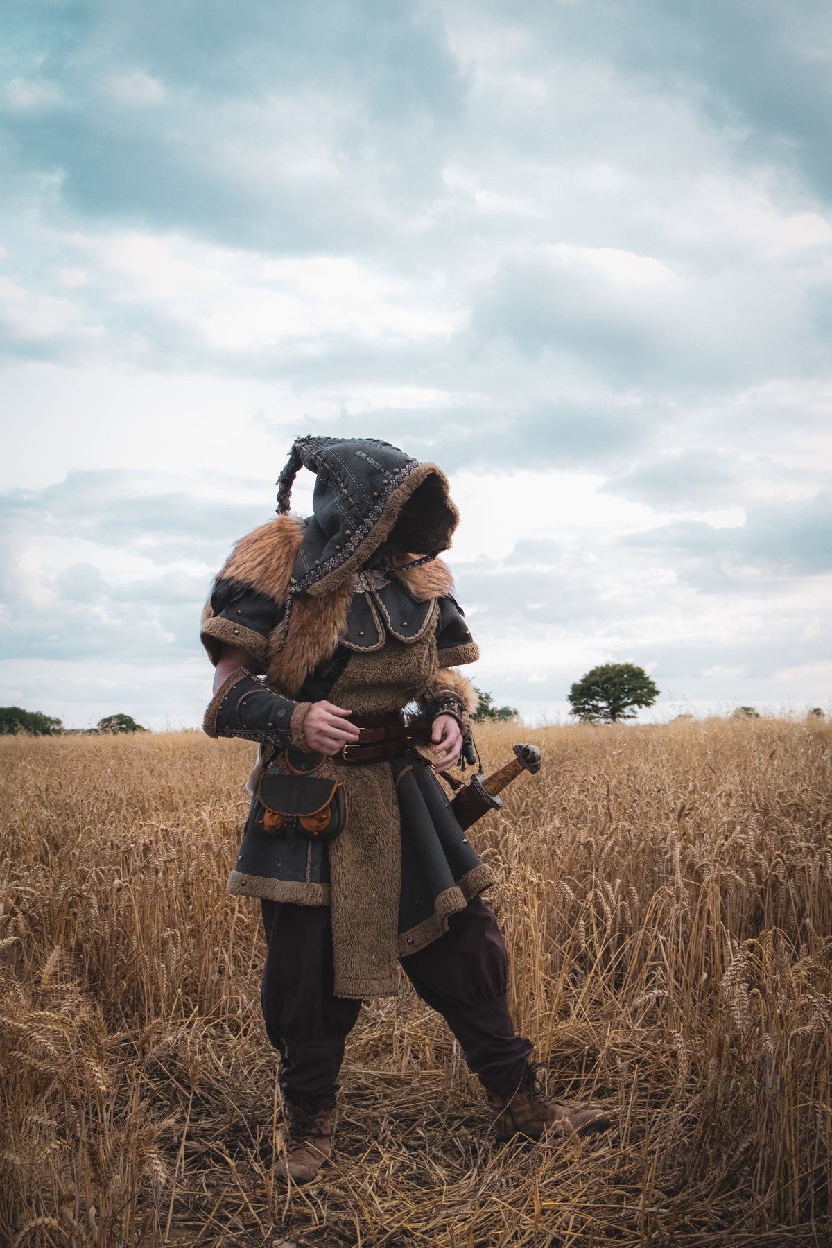 LARP barbarian set with fur tunic, dark hood, and vambraces in a field scene.