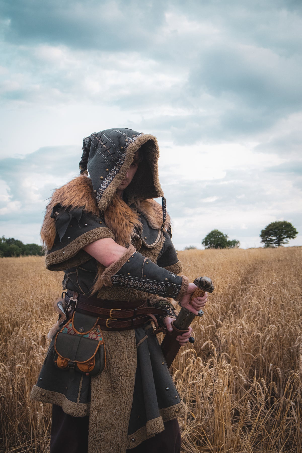 Medieval LARP costume side view featuring a brown faux leather tunic, hood and vambraces.