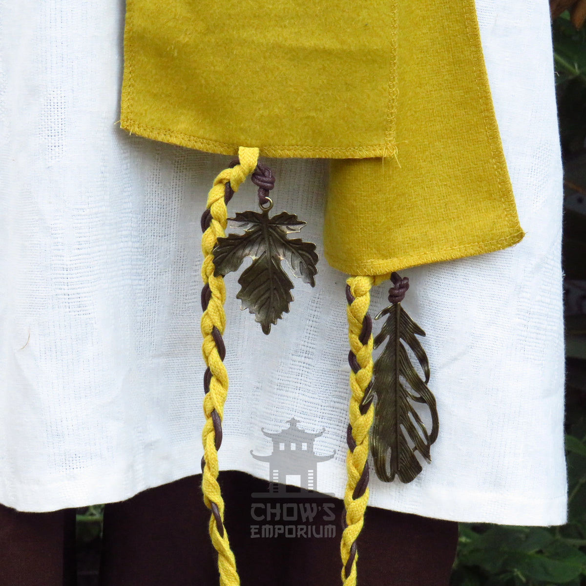 Metal leaf and feather charm on the leather-look cord of the ochre wool sash