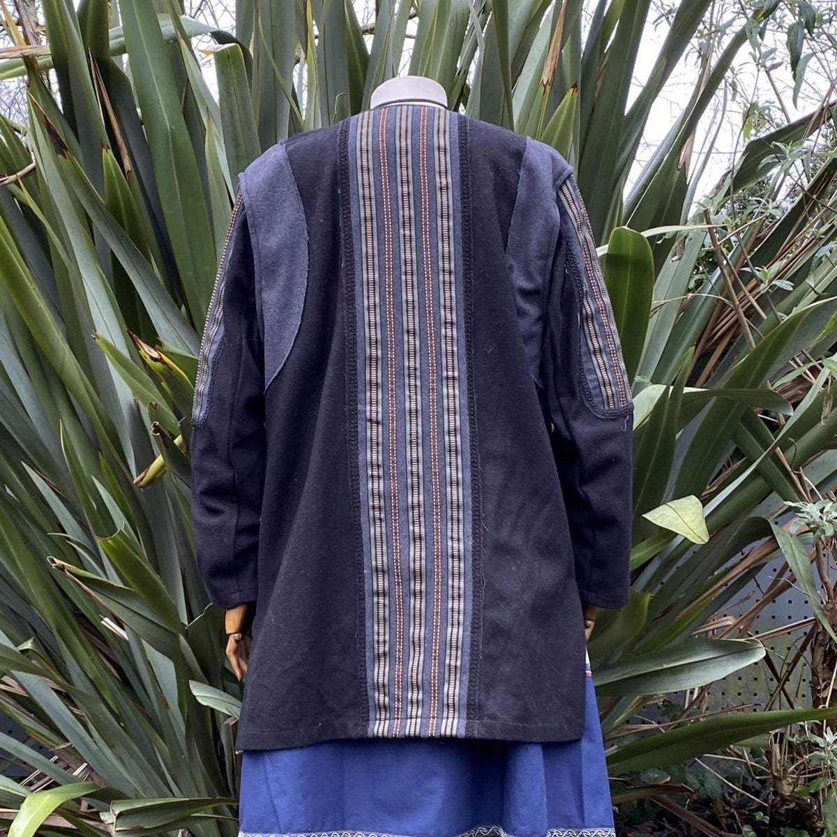 Rear view of black LARP jacket with striped panel, surrounded by greenery.