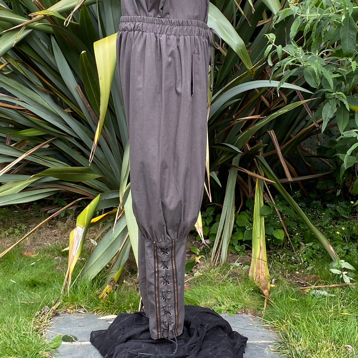 Dark medieval LARP pants with lace-up detail, shown against greenery.