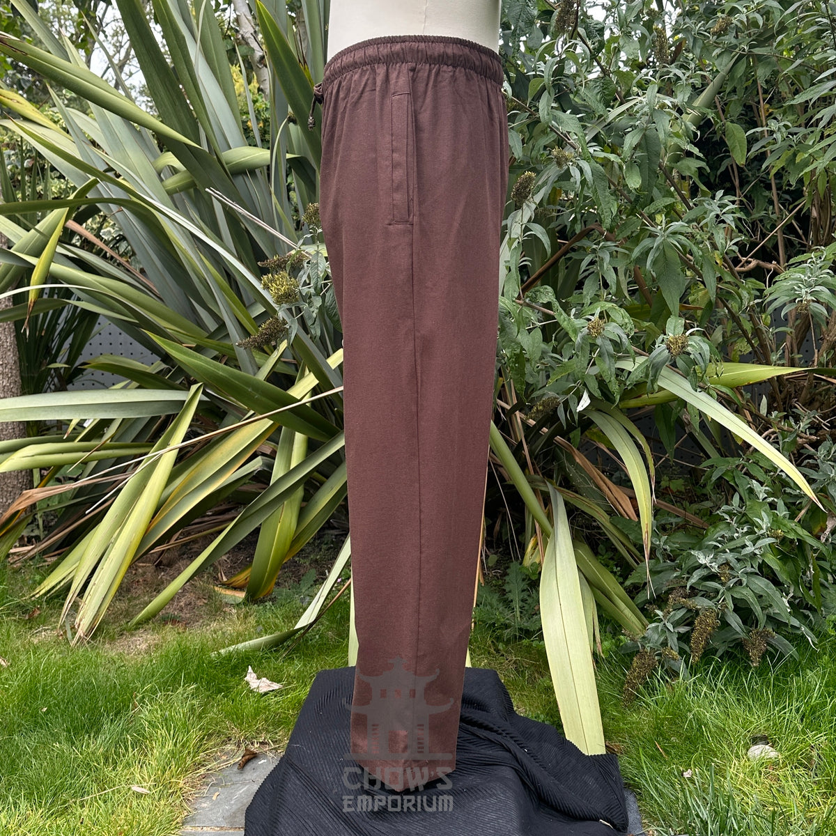 Brown pants on a mannequin against a natural background with green plants.