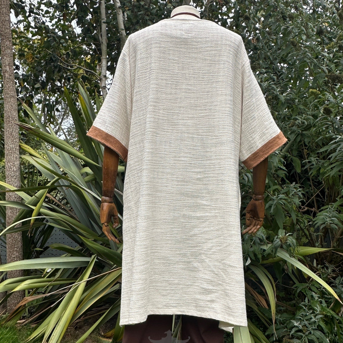 Woven medieval tunic, white with brown trim, back view.
