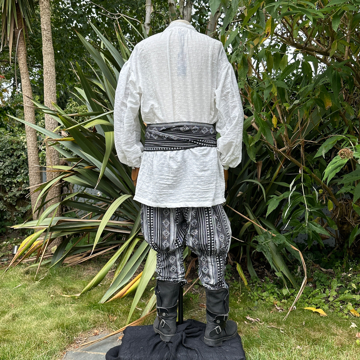 Medieval LARP outfit back view, featuring a white shirt, black and white trousers and matching sash.