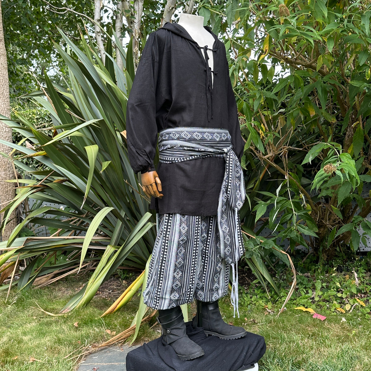 LARP medieval outfit: black hooded shirt, striped pants, and sash, side view.