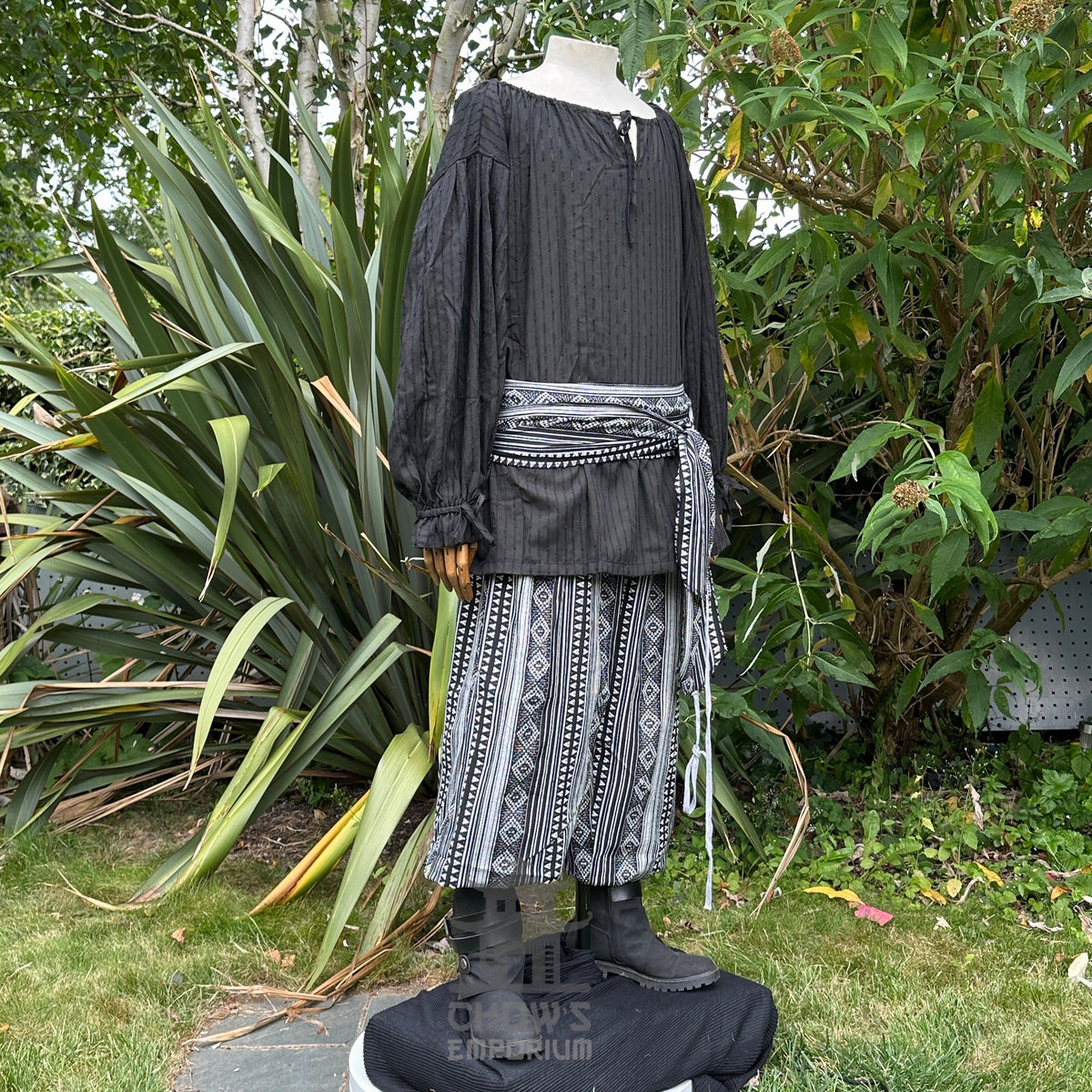 Medieval LARP outfit side view, featuring a black shirt, patterned trousers and sash.