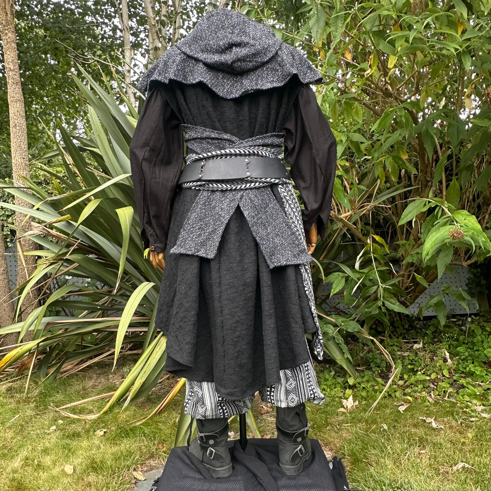 Medieval LARP costume back view, includes black and white waistcoat with asymmetrical front panel and matching sash, wool hood, shirt, and trousers for Renaissance Faire and roleplay events.