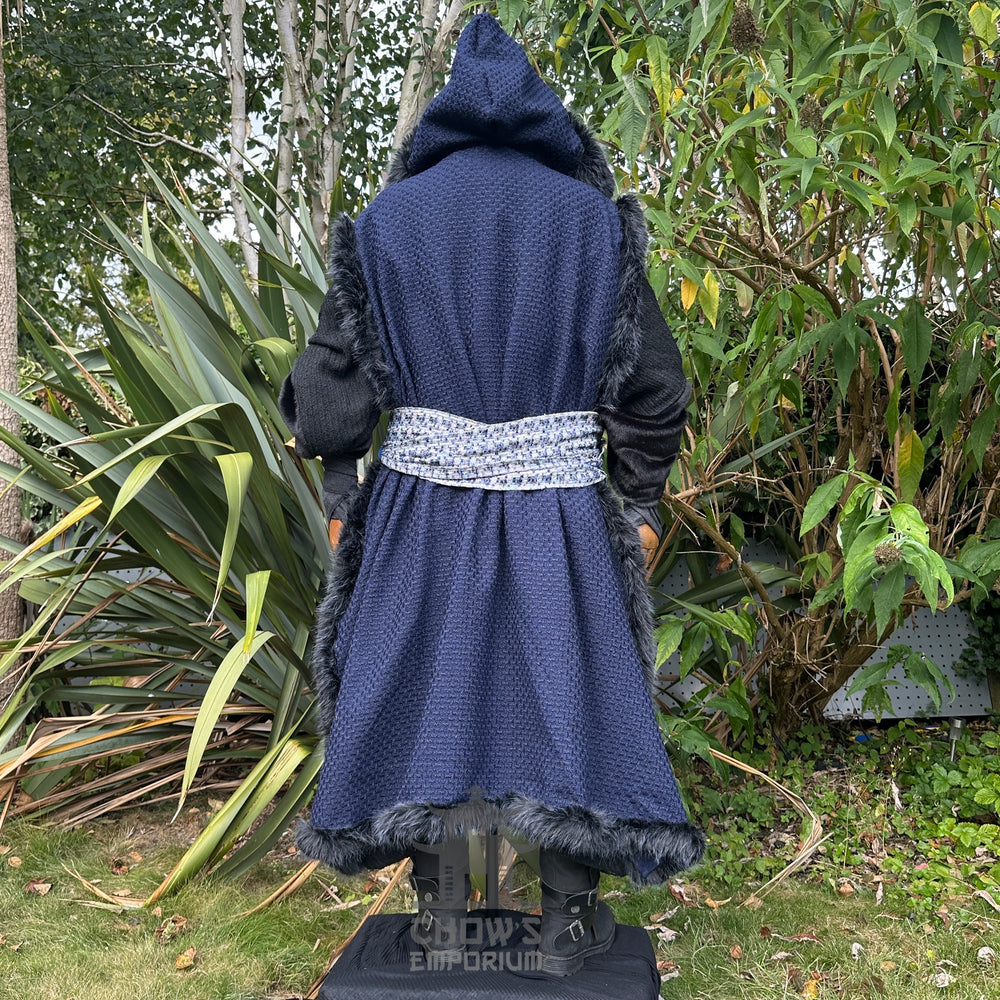 Medieval LARP costume back view, featuring a blue faux fur trim hooded cape, black high collared robe, and sash. For Renaissance Faire and historical roleplay events.