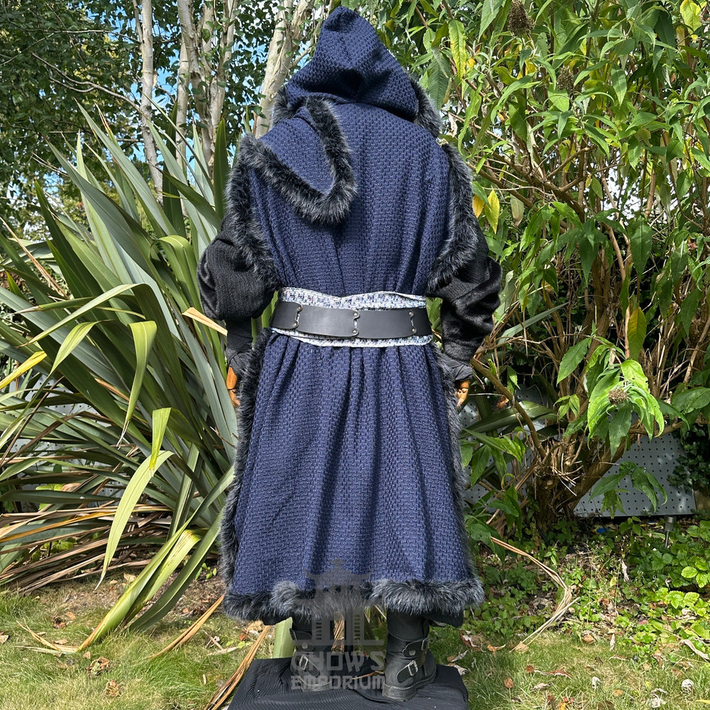 Medieval LARP costume back view, featuring a blue faux fur trim hooded cape, black high collared robe, arm wraps, leather belt, sash and necklace. For Renaissance Faire and historical roleplay events.