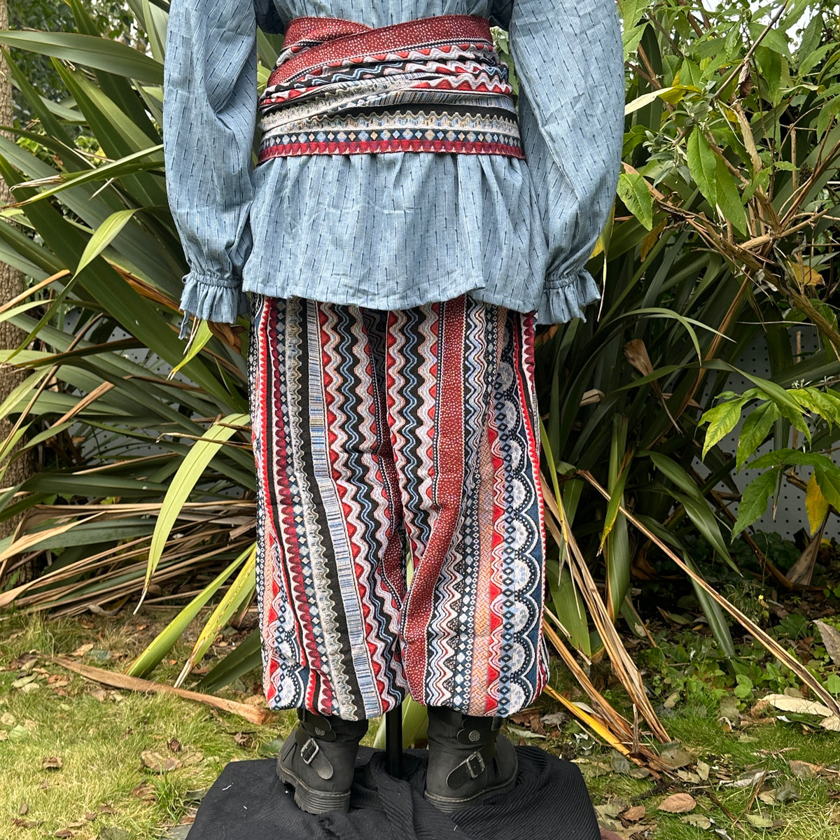 LARP Nordic outfit with blue shirt, red zigzag pants, and sash from behind.
