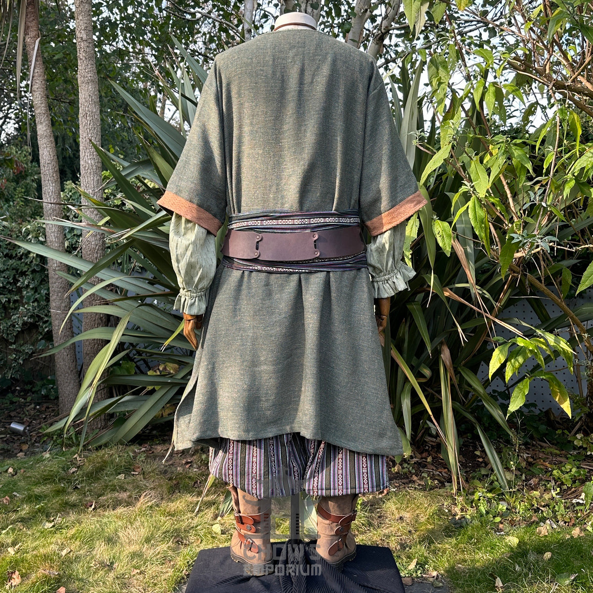 Back view of green medieval LARP tunic, striped pants, sash, leather accents.
