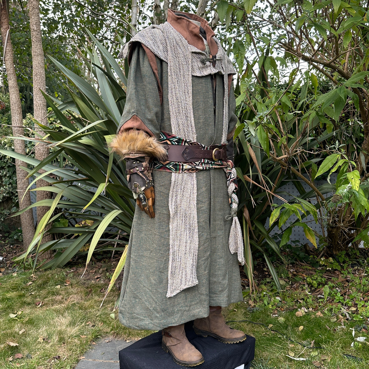 Medieval LARP costume side view featuring green robe, wool hood, vambraces, belt, sash and necklace.