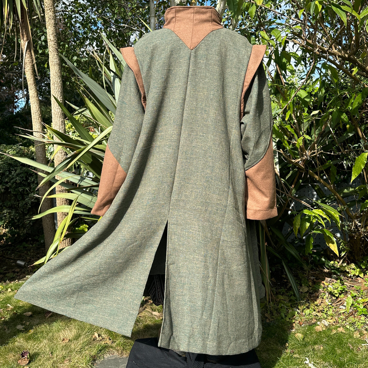 Back view of green medieval robe with brown accents, worn in sunlight.