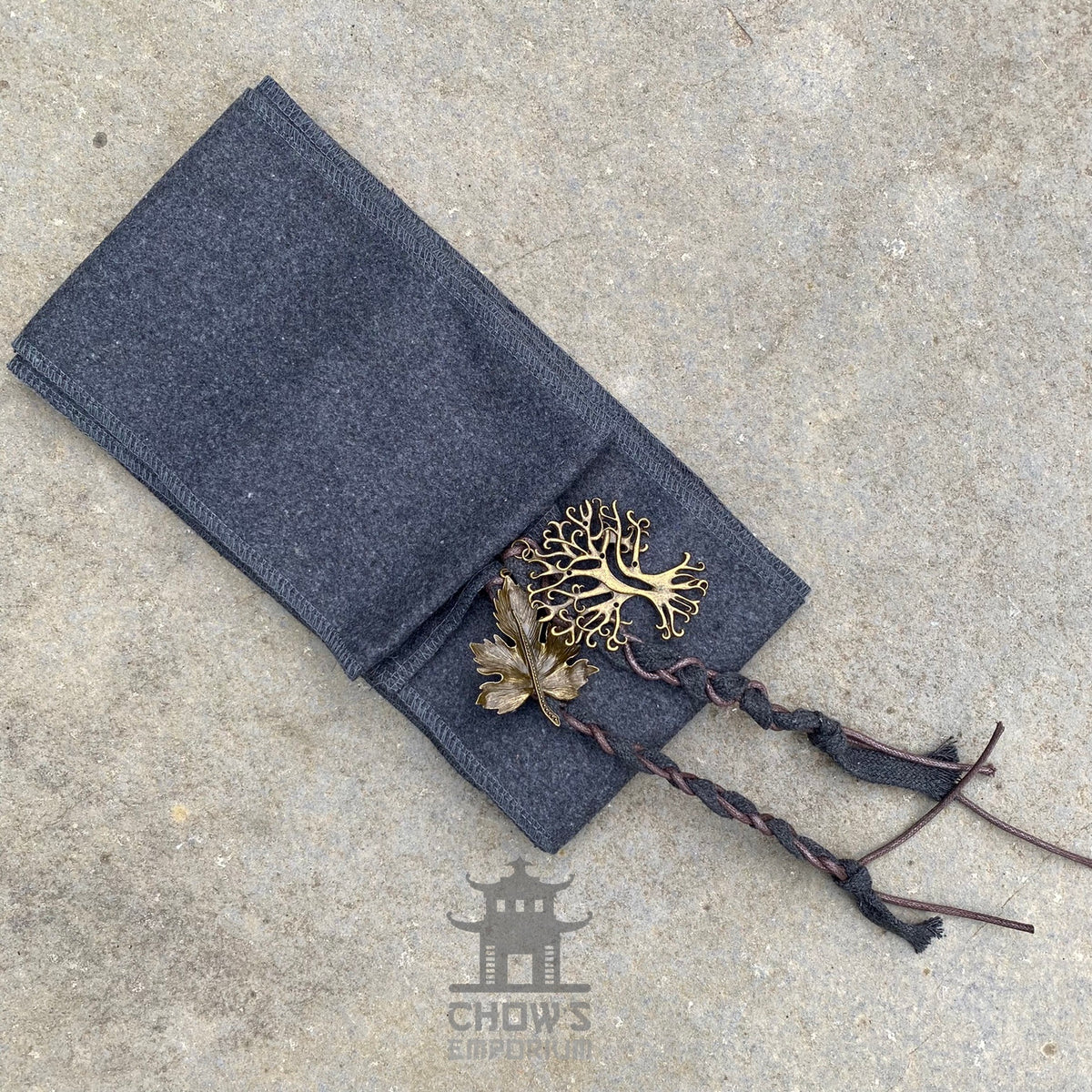 Braided cord and metal leaf on grey LARP hood, stone background.