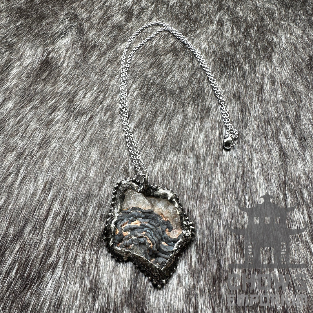 Silver necklace with rough stone pendant on grey fur, medieval style.