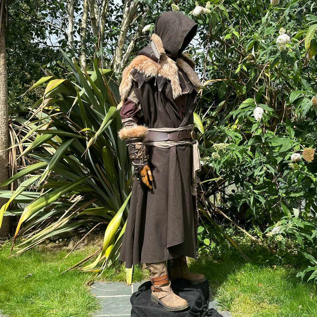 Medieval LARP costume side view featuring brown cloak, faux leather hood, arm wraps and sash.