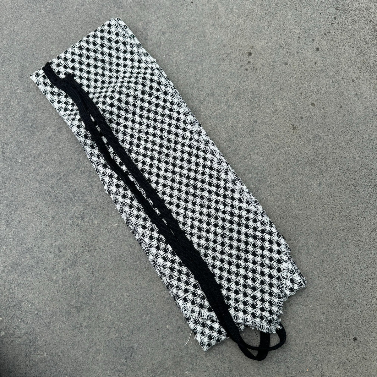 Checkered black and white LARP sash, woven fabric, laid on concrete surface.