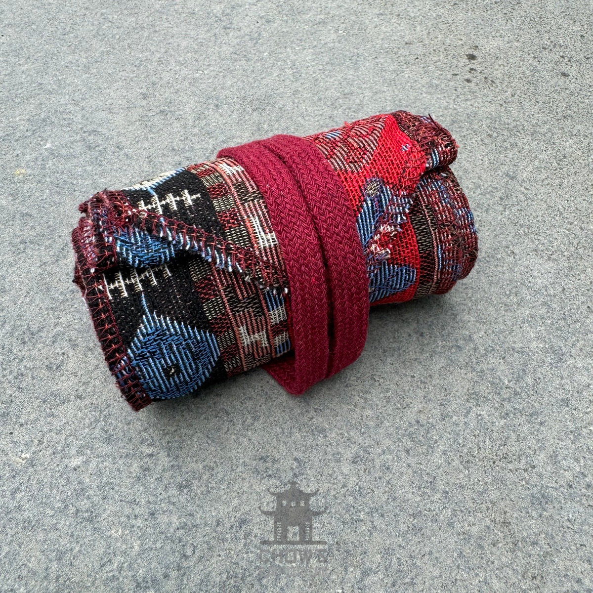 Rolled red Aztec pattern pirate sash for LARP on grey background.