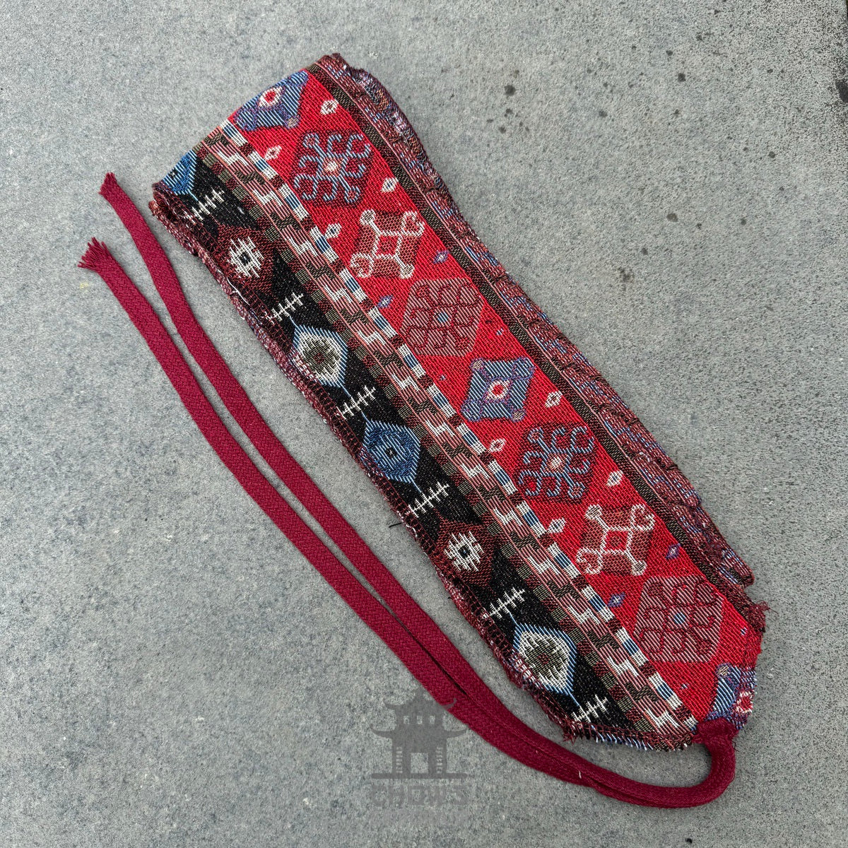 Red and blue patterned LARP pirate sash on textured concrete surface.