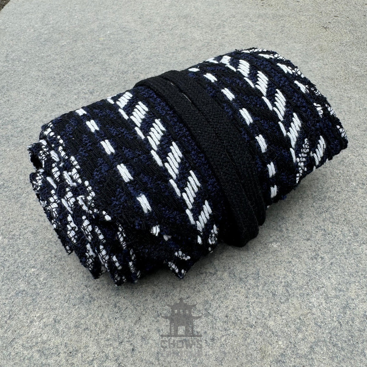 Black, white, and blue herringbone medieval sash rolled on stone surface.