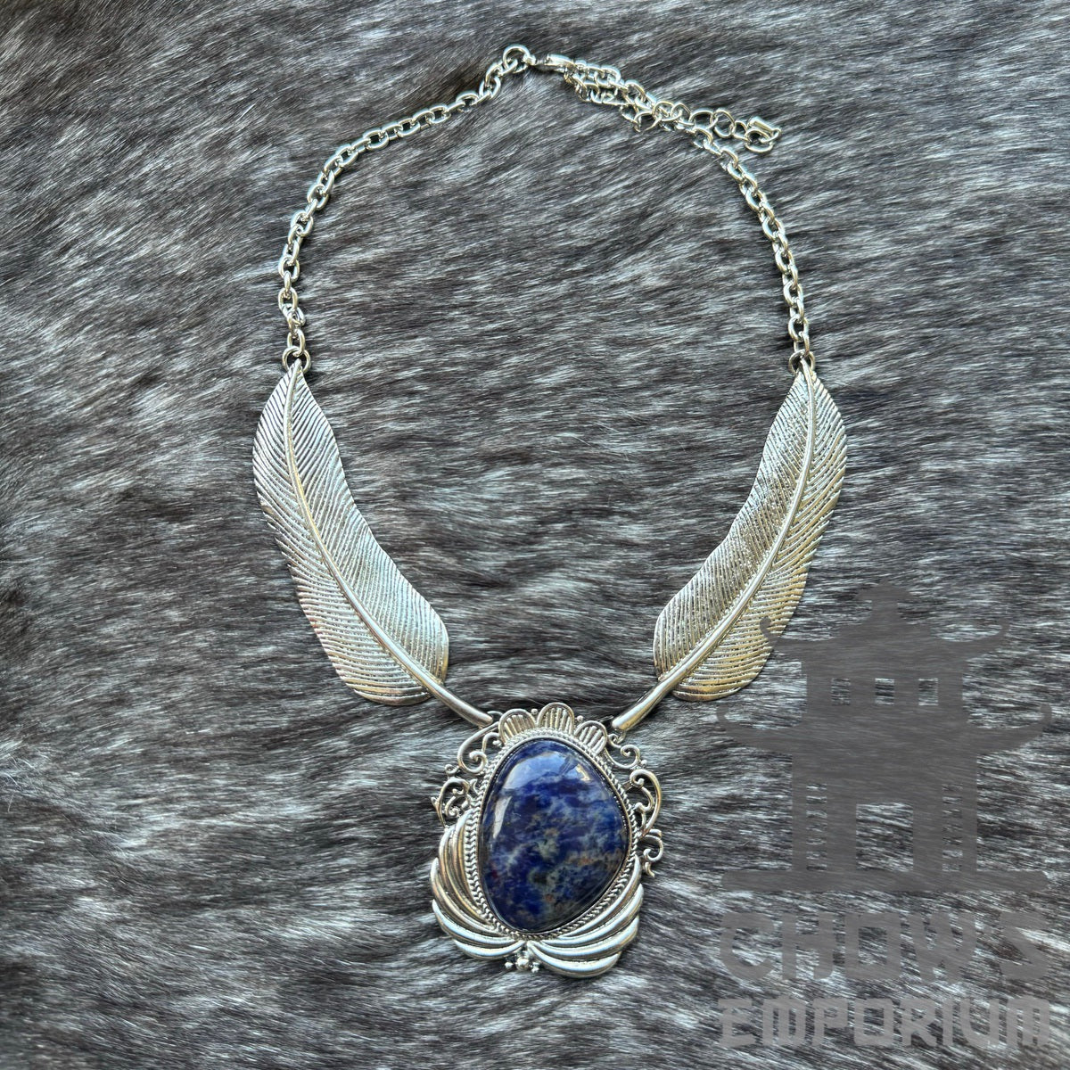 Silver necklace with feather design and blue stone, on a fur background.