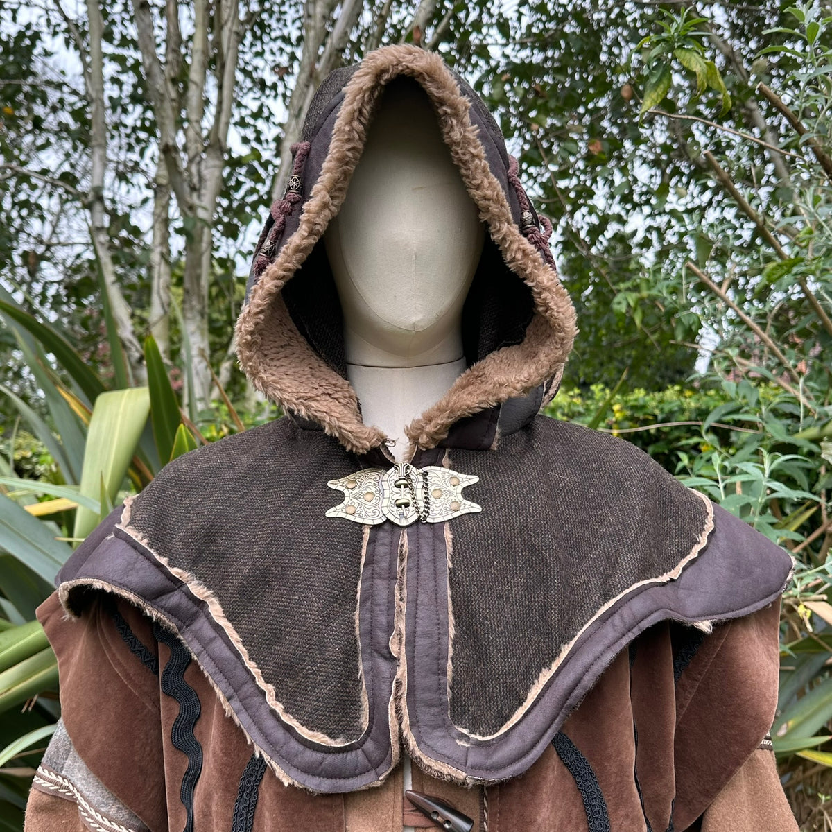 LARP hood with fleece lining and ornate clasp, surrounded by trees.