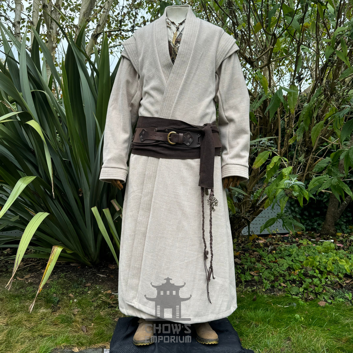 LARP medieval robe front view, beige with brown belt amid garden greenery.