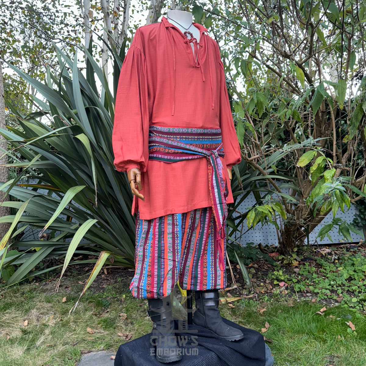 Medieval LARP outfit side view, featuring an orange shirt, multi-striped trousers and matching sash.