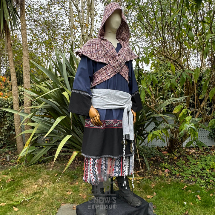 Medieval LARP outfit side view, featuring a blue and black tunic, patterned trousers, and sash. For Renaissance Faire and historical roleplay events.