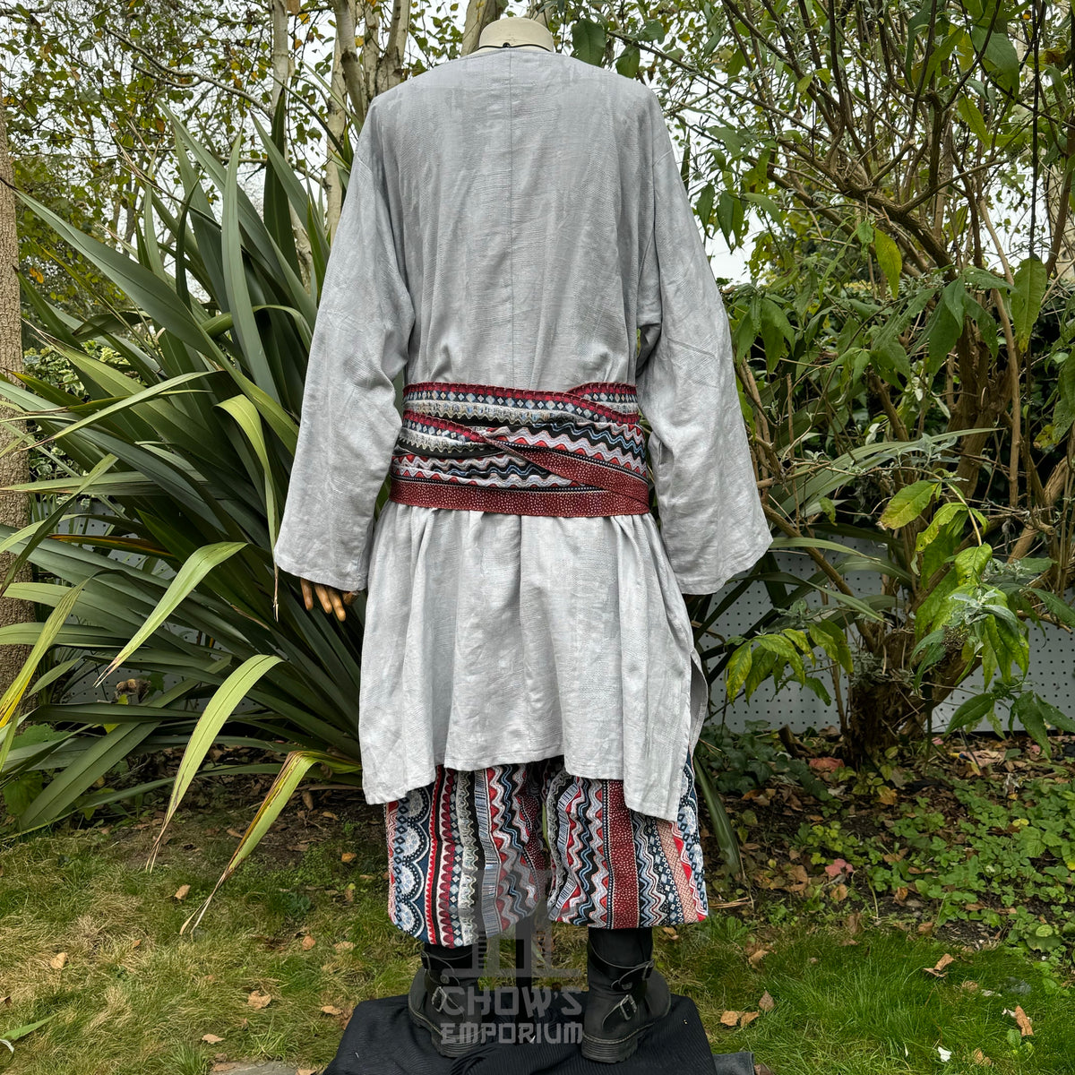 Medieval LARP outfit back view, featuring a grey tunic, multi-striped trousers and matching sash.