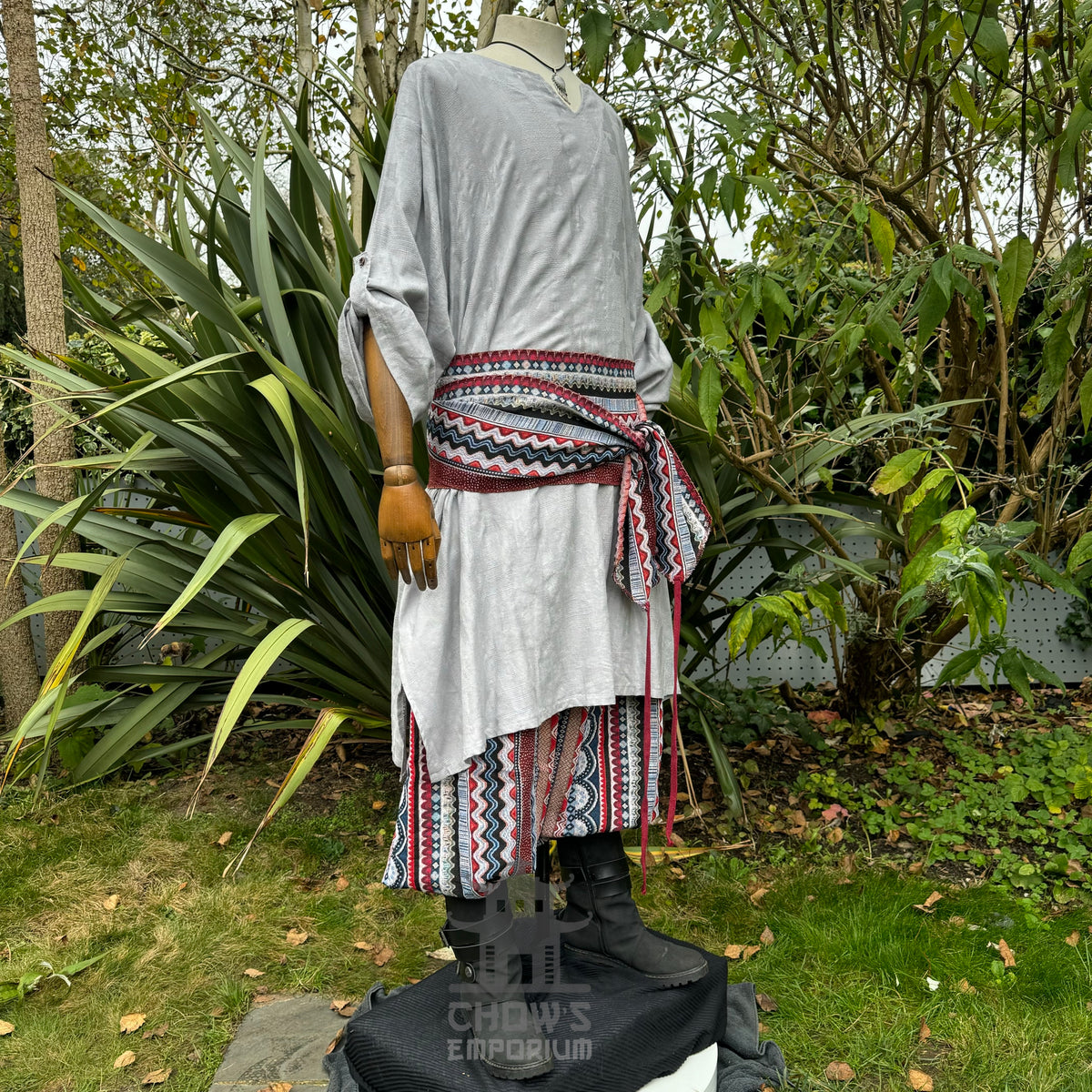 Medieval LARP outfit side view, featuring a grey tunic, multi-striped trousers and matching sash.