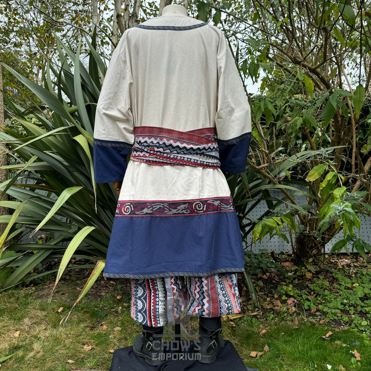 Back view of medieval robe in cream and blue with patterned trim, on display.