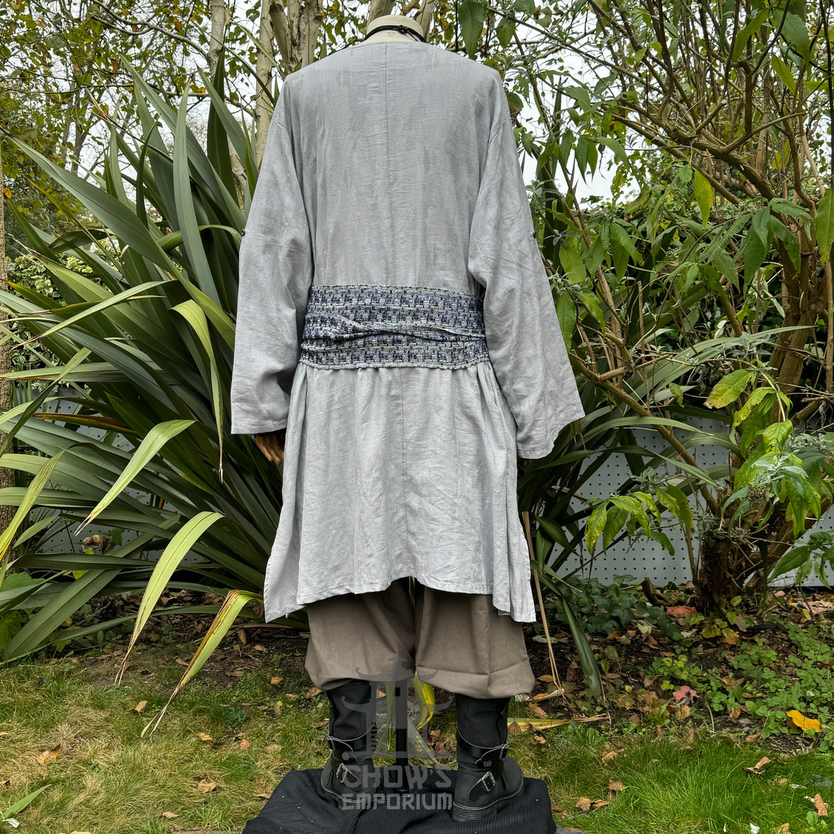 Grey tunic with sash, medieval LARP style, back view amidst green foliage.